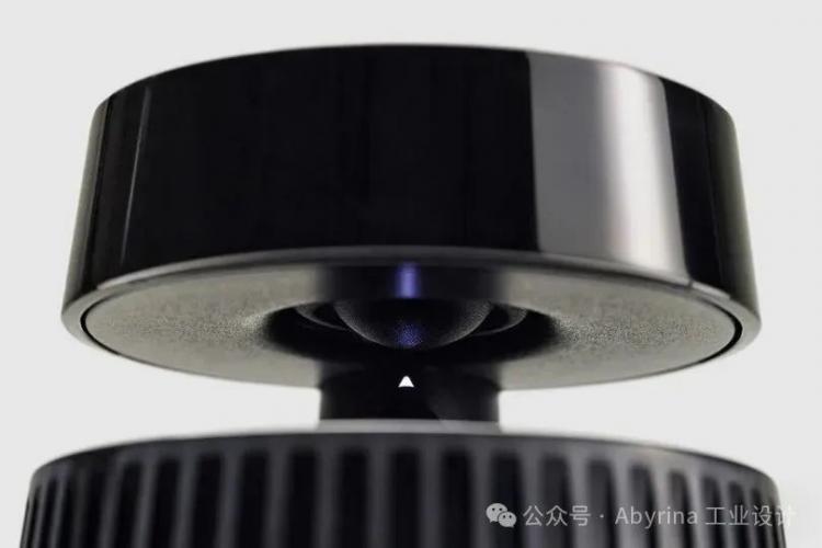 Close-up of a black Bang & Olufsen electronic device with a circular top section suspended above a base, featuring a small triangular indicator and a smooth, reflective surface.