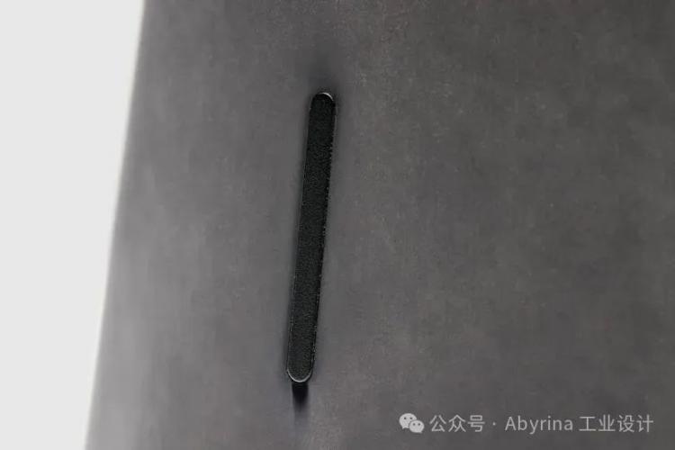 A close-up of a vertical black slit or slot on a smooth, gray surface, reminiscent of the minimalist design often seen in Bang & Olufsen products.