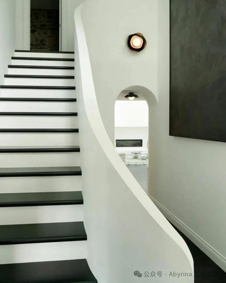 A modern interior with a white staircase featuring black treads, curved railing, white walls, and minimalist light fixtures.