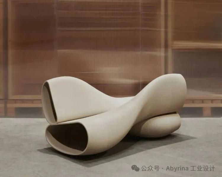 A modern, sculptural beige bench with smooth curves and hollowed ends sits on a concrete floor against a blurred brown background.