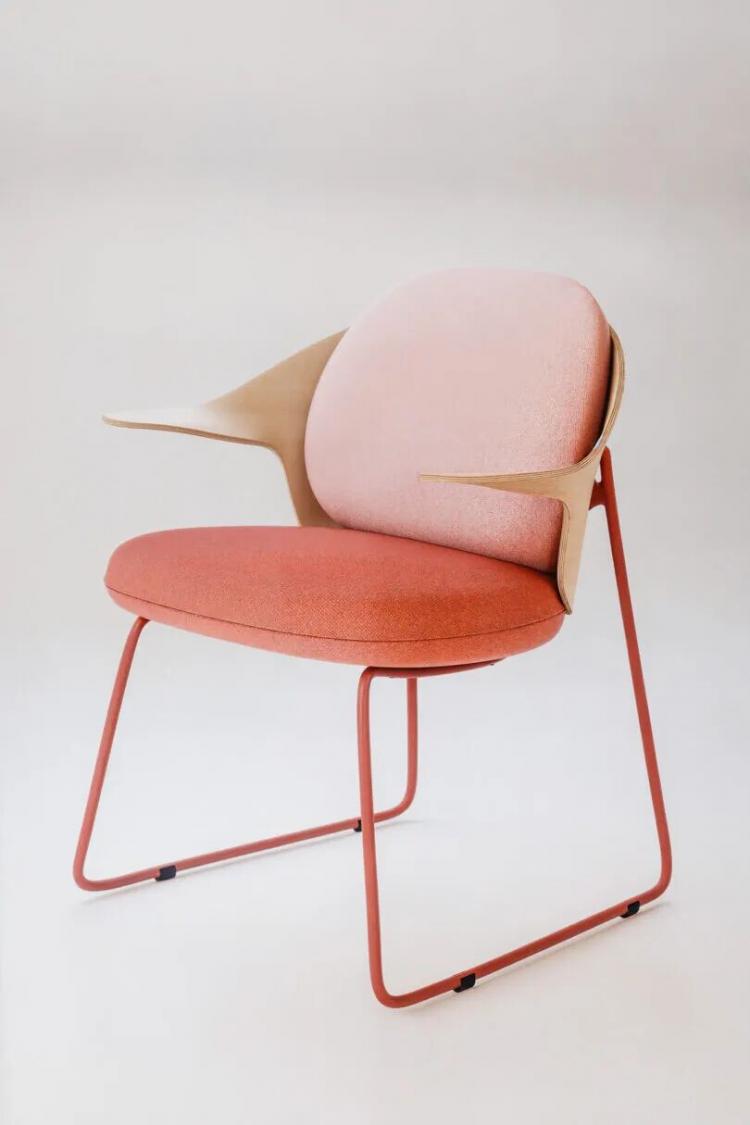 Modern chair with a pink cushioned seat and backrest, tan armrests, and a red metal frame, set against a plain light background.