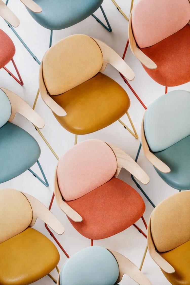 An overhead view of multiple pastel-colored chairs with curved wooden armrests and metal legs arranged closely together in a pattern.