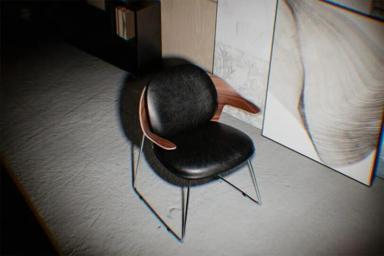 A modern black chair with wooden armrests sits on a textured floor next to a wall with framed art and books on a shelf.