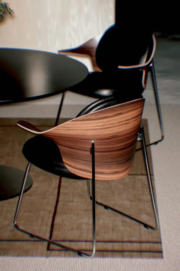Two modern wooden chairs with black seats and metal legs are positioned around a round black table on a beige carpet.