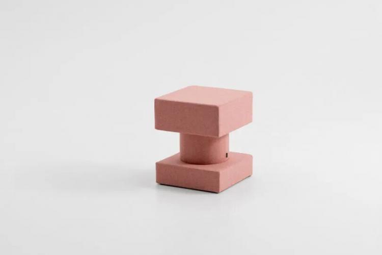 A modern, pink, geometric stool with a cylindrical center and two square-shaped cushions, photographed against a plain white background.