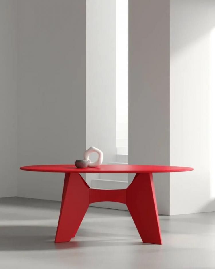A modern, red round table with geometric legs stands in a minimalist room near a window, holding a white pitcher and a cup