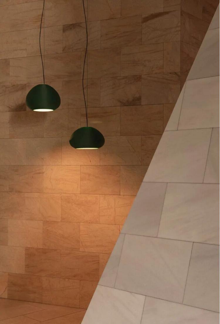 Two green pendant lights hang against a tan stone-tiled wall, with a large diagonal white-tiled structure in the foreground.