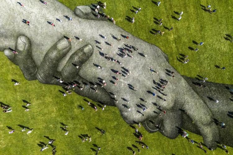 无人机拍摄的画面显示，在明尼阿波利斯的一片大草坪上，两只巨大的手臂紧紧相握，周围有几十个人在走动。